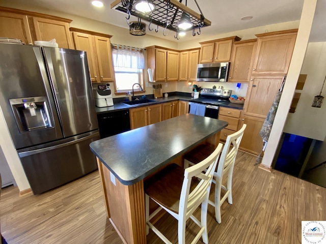 kitchen featuring appliances with stainless steel finishes, dark countertops, light wood-type flooring, and a sink