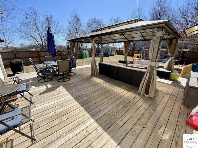 deck with a fenced backyard, a storage unit, an outbuilding, and outdoor dining space