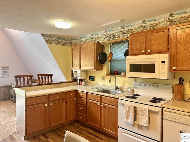 kitchen with brown cabinets, a sink, white appliances, a peninsula, and light countertops