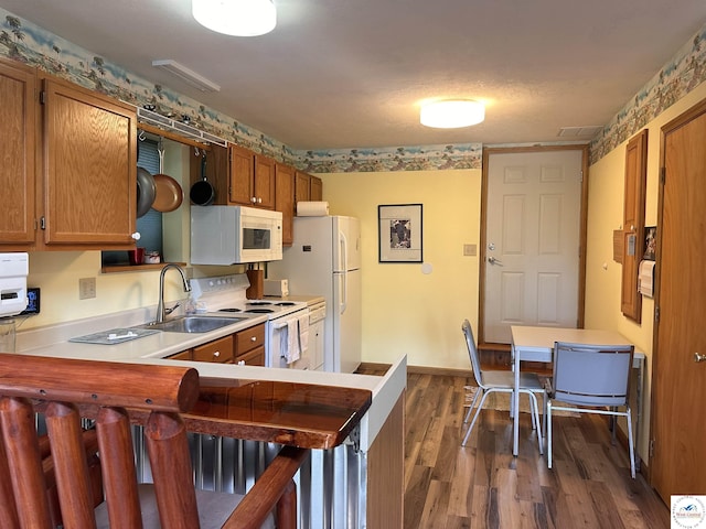 kitchen with dark wood-style floors, a sink, brown cabinets, white appliances, and light countertops