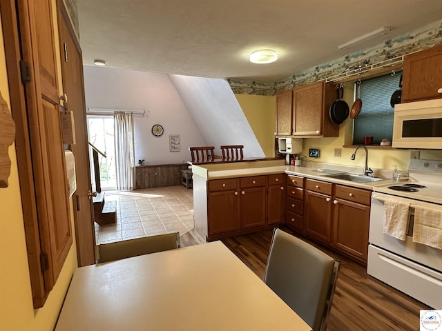 kitchen with dark wood-style flooring, a sink, white appliances, a peninsula, and light countertops