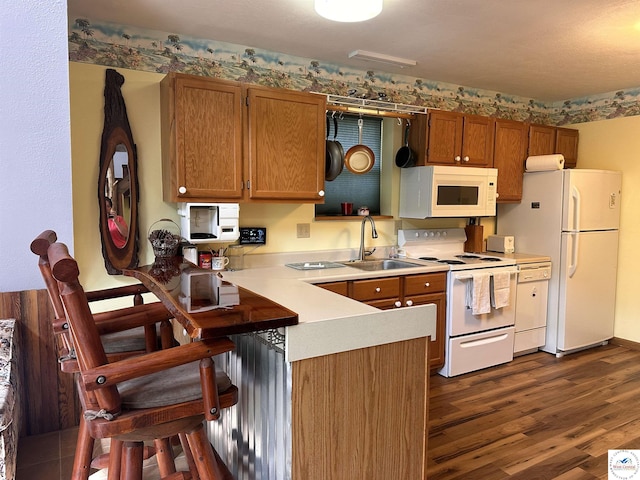 kitchen featuring white appliances, brown cabinetry, light countertops, a sink, and a peninsula