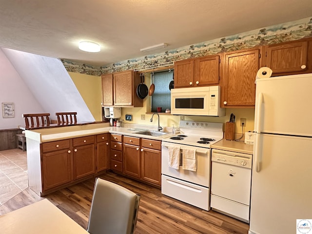 kitchen with brown cabinetry, white appliances, a peninsula, and a sink