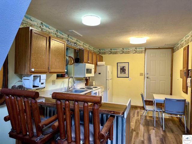 kitchen featuring wood finished floors, white appliances, brown cabinetry, light countertops, and a sink