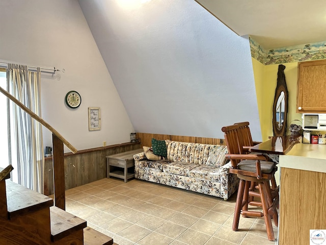 living room featuring a wainscoted wall, light tile patterned flooring, and vaulted ceiling