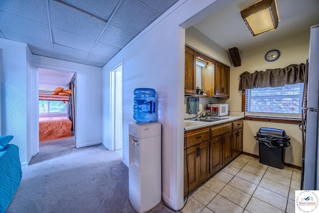 kitchen with light countertops, brown cabinets, white appliances, a paneled ceiling, and a sink