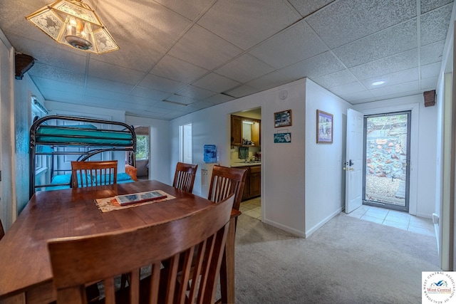 dining area featuring light colored carpet, baseboards, and a paneled ceiling