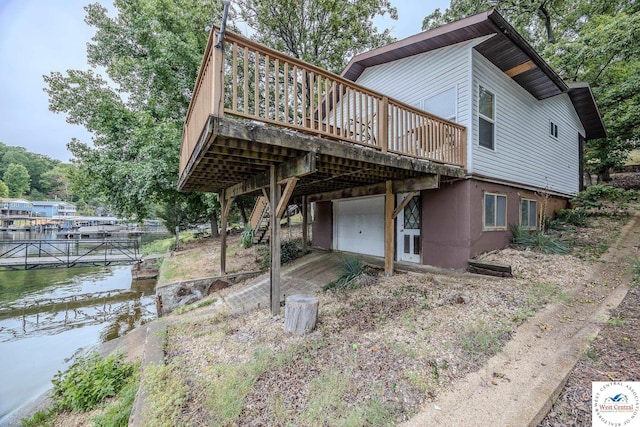 back of property featuring stairs, an attached garage, a deck with water view, and driveway