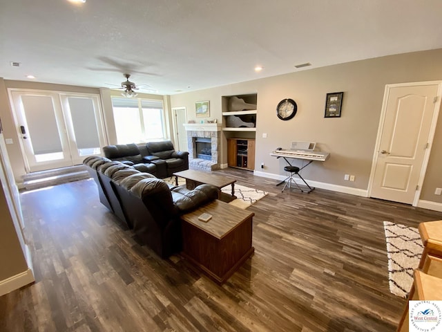 living area with a fireplace with raised hearth, ceiling fan, wood finished floors, visible vents, and baseboards