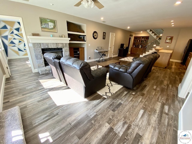 living room with wood finished floors, a stone fireplace, baseboards, and stairs