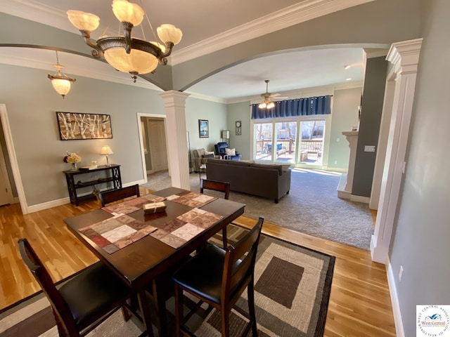 dining space featuring arched walkways, ceiling fan with notable chandelier, wood finished floors, ornamental molding, and ornate columns