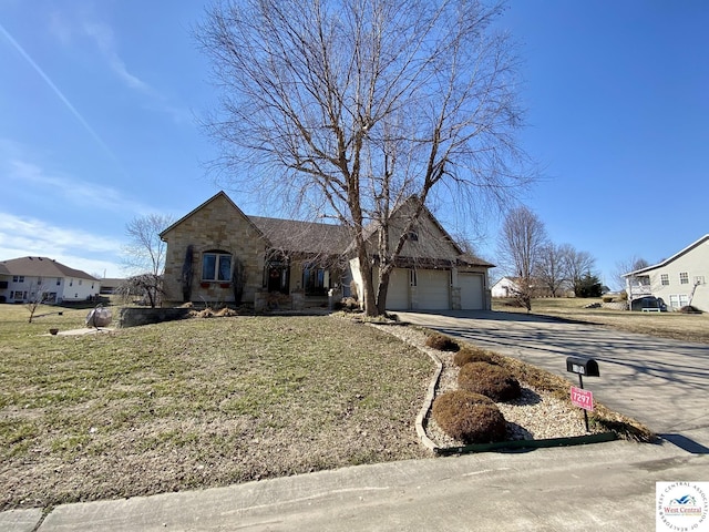 view of front of house with stone siding, a front lawn, an attached garage, and driveway