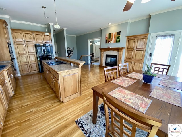 kitchen with a glass covered fireplace, ornamental molding, a center island, light wood-type flooring, and black appliances