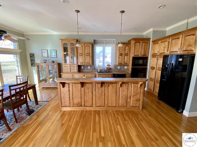 kitchen featuring brown cabinets, light wood finished floors, backsplash, black appliances, and a kitchen breakfast bar