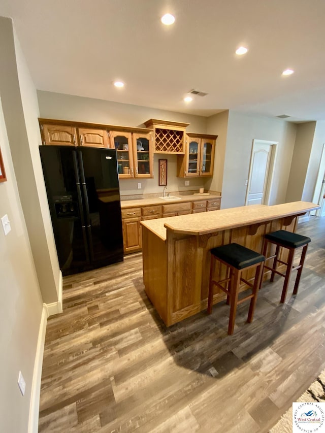 kitchen featuring light wood-type flooring, light countertops, black fridge with ice dispenser, and a breakfast bar area