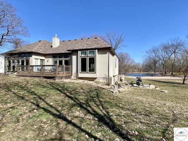 back of property with roof with shingles, a chimney, a lawn, and a deck with water view