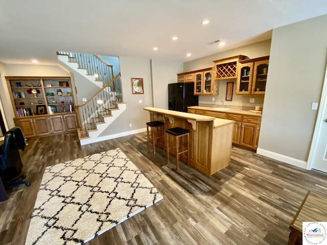 kitchen with light countertops, black fridge with ice dispenser, a kitchen island, a sink, and a kitchen breakfast bar