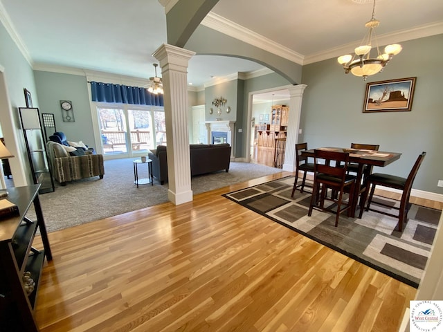 dining area with arched walkways, a fireplace, ornate columns, wood finished floors, and baseboards