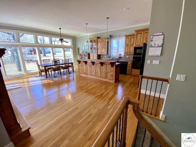 kitchen featuring decorative backsplash, light wood-style flooring, a kitchen breakfast bar, crown molding, and black appliances