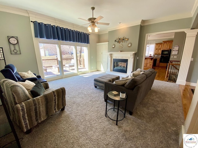 living room with ornamental molding, a glass covered fireplace, ornate columns, and a ceiling fan