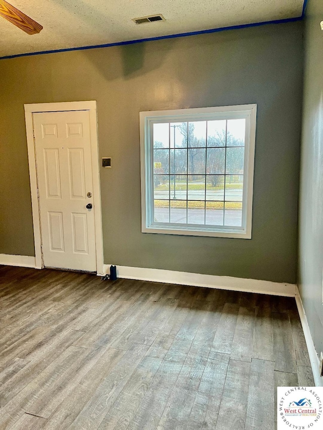 unfurnished room featuring light wood-style flooring, a textured ceiling, visible vents, and baseboards