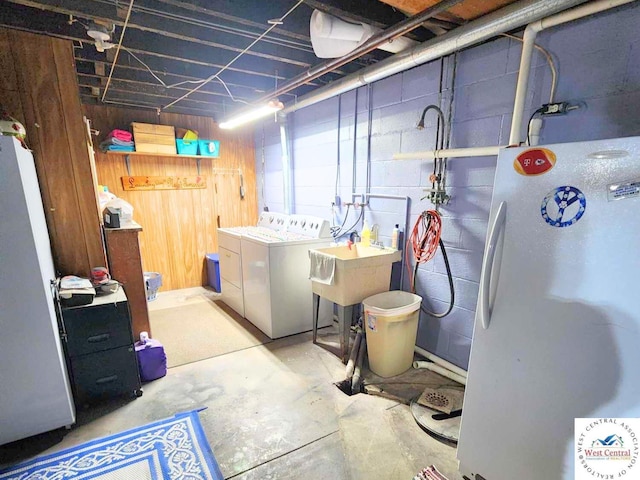 unfinished basement featuring a sink, concrete block wall, washer and dryer, and freestanding refrigerator