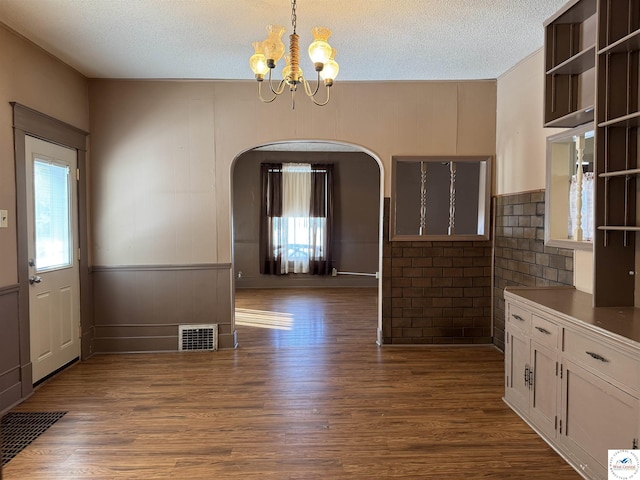 unfurnished dining area with dark wood-type flooring, arched walkways, a wealth of natural light, and visible vents