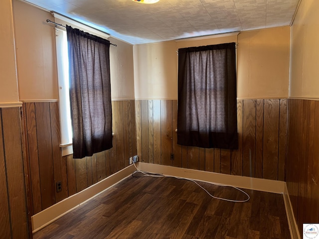 spare room with dark wood-type flooring, wood walls, and wainscoting