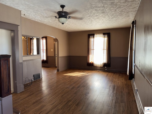 spare room featuring a wainscoted wall, dark wood-type flooring, arched walkways, and visible vents