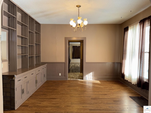 unfurnished dining area featuring a textured ceiling, a wainscoted wall, wood finished floors, visible vents, and an inviting chandelier