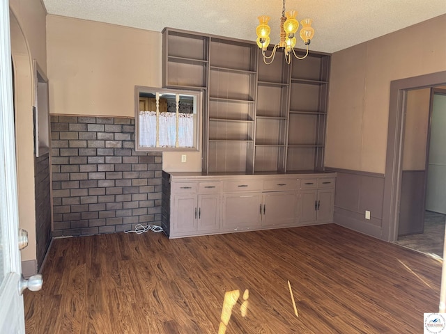 unfurnished dining area with a chandelier, dark wood-style flooring, wainscoting, and a textured ceiling