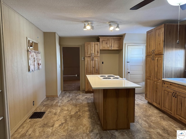 kitchen with a center island, visible vents, light countertops, white electric cooktop, and brown cabinetry