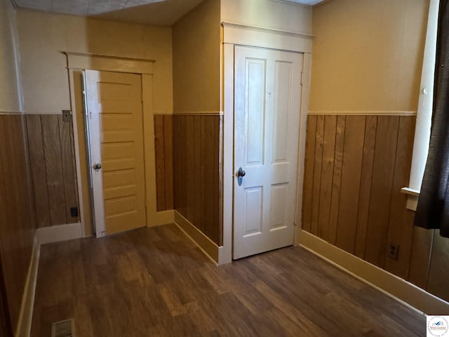 entryway featuring dark wood-style flooring, wood walls, wainscoting, and visible vents