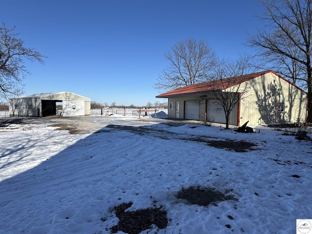 yard layered in snow with a garage, an outdoor structure, and an outbuilding