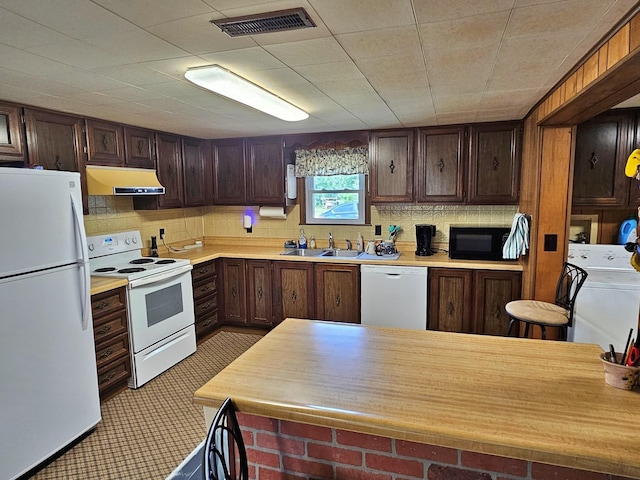 kitchen featuring white appliances, washer / clothes dryer, light countertops, under cabinet range hood, and a sink