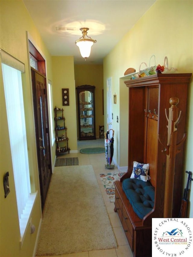 hallway featuring light tile patterned floors, baseboards, and visible vents