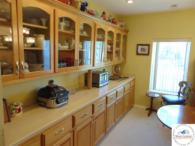 kitchen with light countertops, glass insert cabinets, visible vents, and baseboards