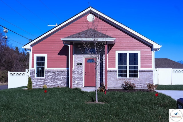 view of front facade with brick siding, a front yard, and fence