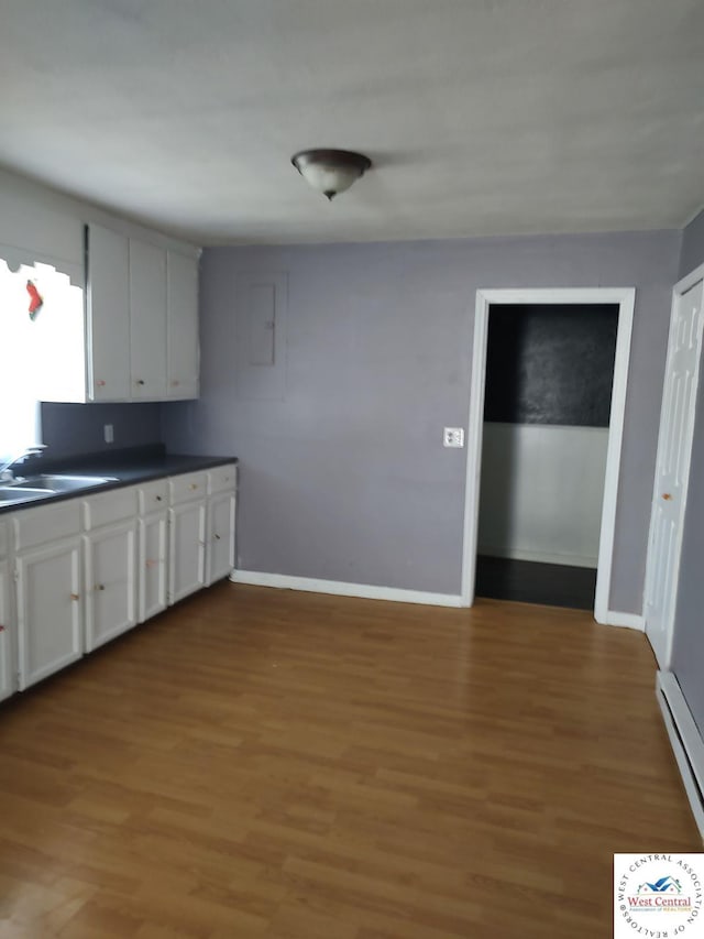 kitchen with dark countertops, dark wood-style floors, baseboard heating, white cabinetry, and a sink