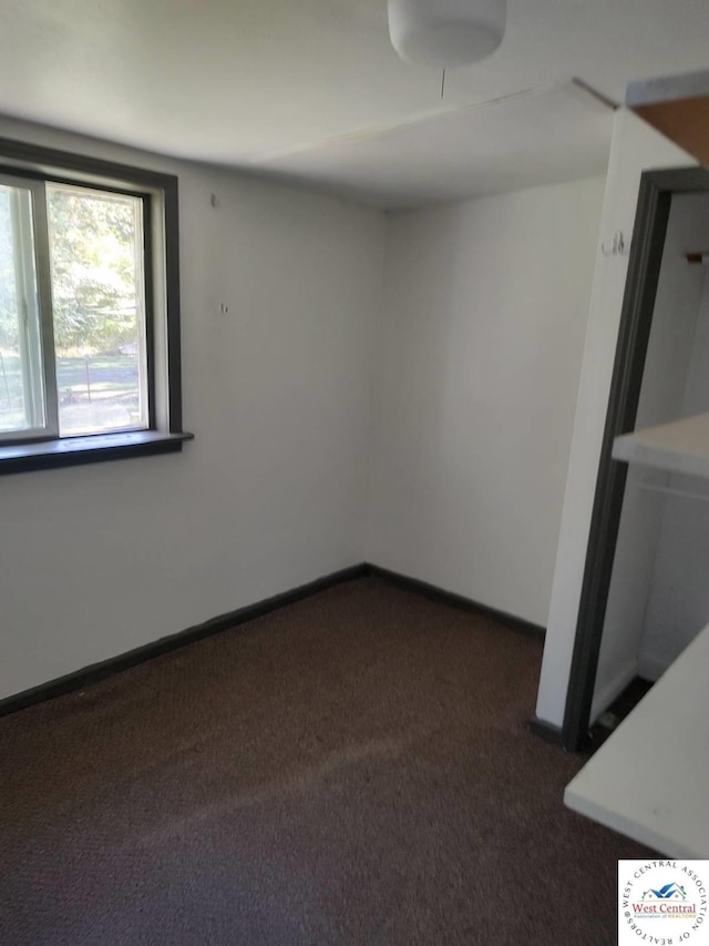 spare room with dark carpet and baseboards