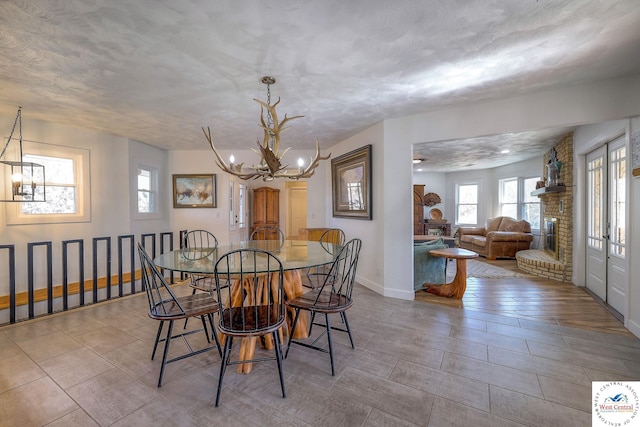 dining room with an inviting chandelier, a brick fireplace, baseboards, and a textured ceiling