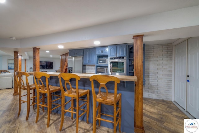 kitchen featuring a kitchen bar, dark wood-type flooring, blue cabinetry, appliances with stainless steel finishes, and a peninsula