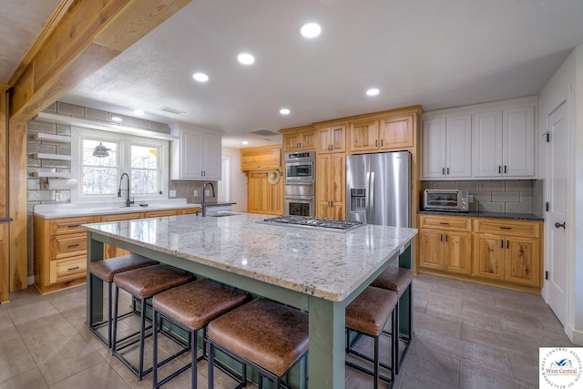 kitchen featuring visible vents, an island with sink, a sink, stainless steel appliances, and decorative backsplash