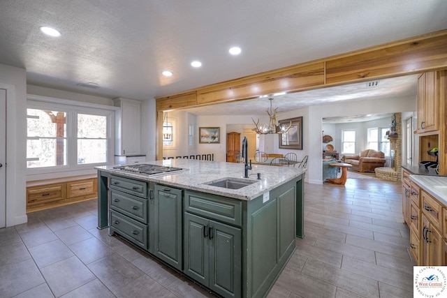 kitchen featuring a kitchen island with sink, a sink, open floor plan, green cabinets, and stainless steel gas cooktop