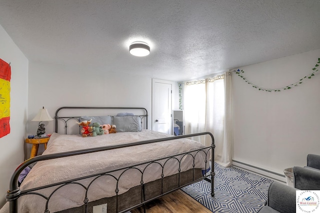 bedroom with a textured ceiling, a baseboard heating unit, and wood finished floors