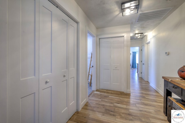 hallway with light wood-style flooring, baseboards, and visible vents