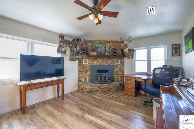 office space with wood finished floors, baseboards, visible vents, a wood stove, and ceiling fan