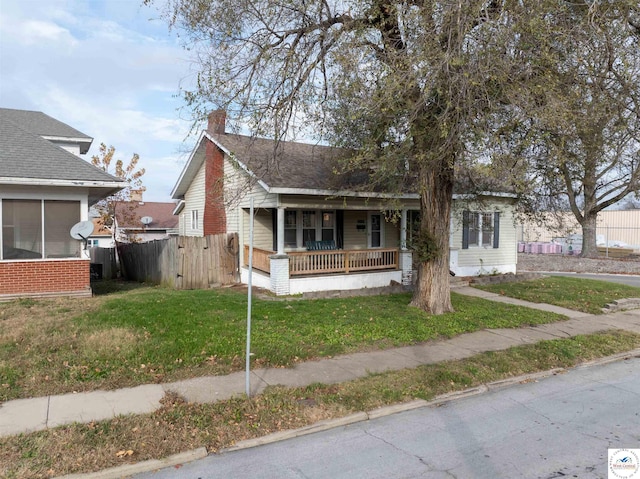 bungalow featuring a front yard, covered porch, fence, and a chimney