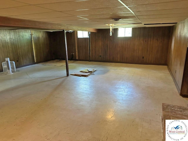 basement featuring wood walls, a drop ceiling, and light floors