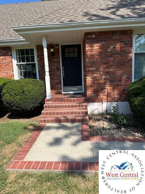 doorway to property featuring roof with shingles and brick siding